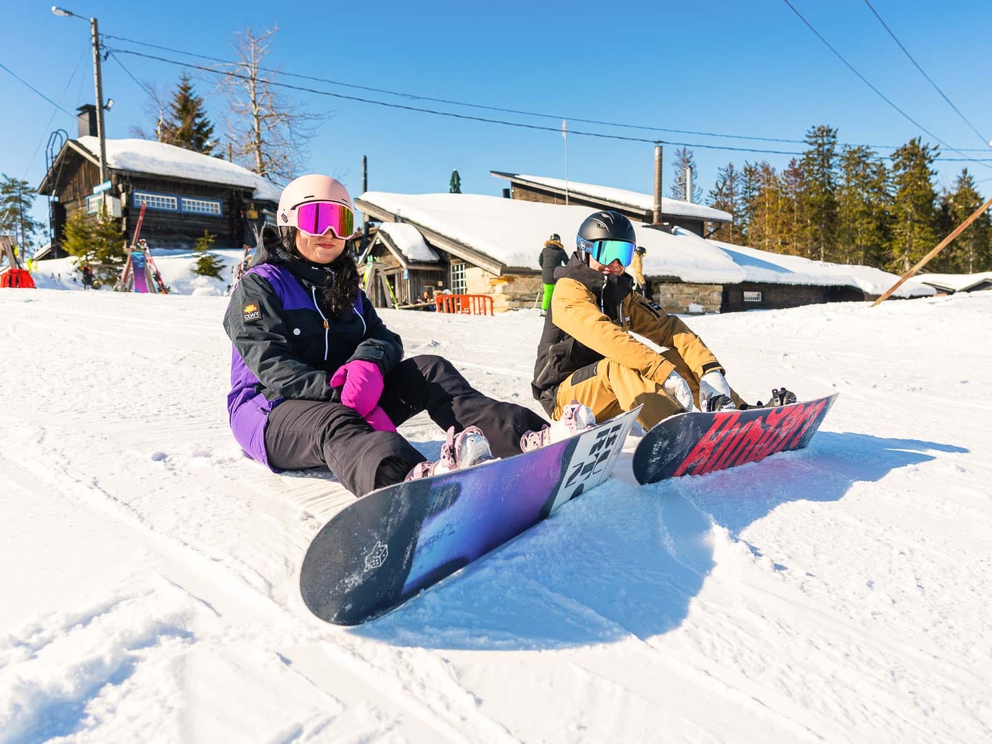 Lumilautailijat istumassa rinteessä.